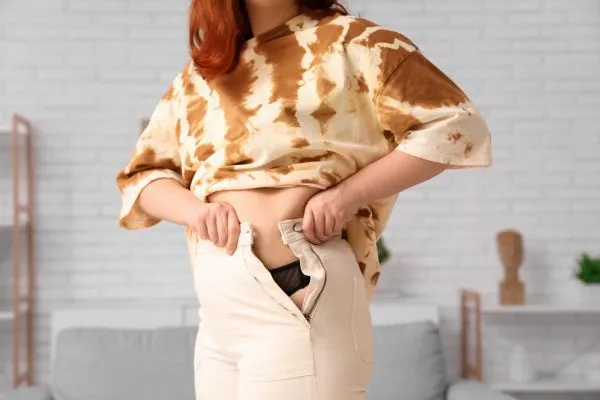 Image of woman trying to do her trousers up after pregnancy weight gain Teddington