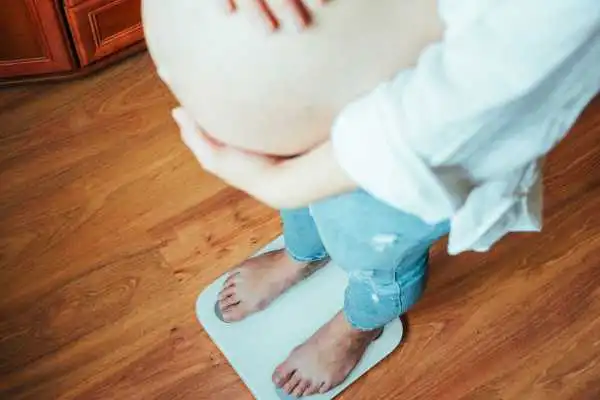 Image of woman weighing herself and experiencing weight gain through pregnancy Teddington